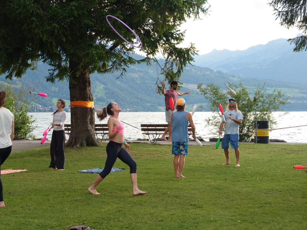 The MOVE Interlaken group in action at Kifferinseli. A girl plays with a hoop, some people are juggling with clups and a gui is on the slackline. 